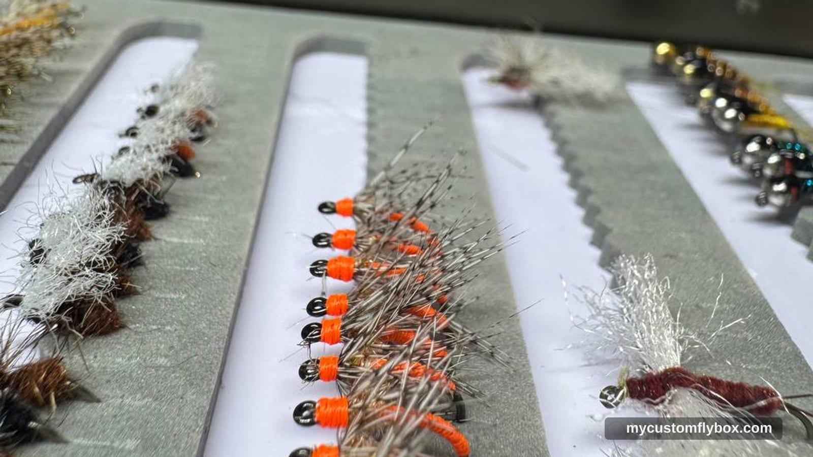 Rows of hand-tied trout flies arranged in a fly box at the tying bench