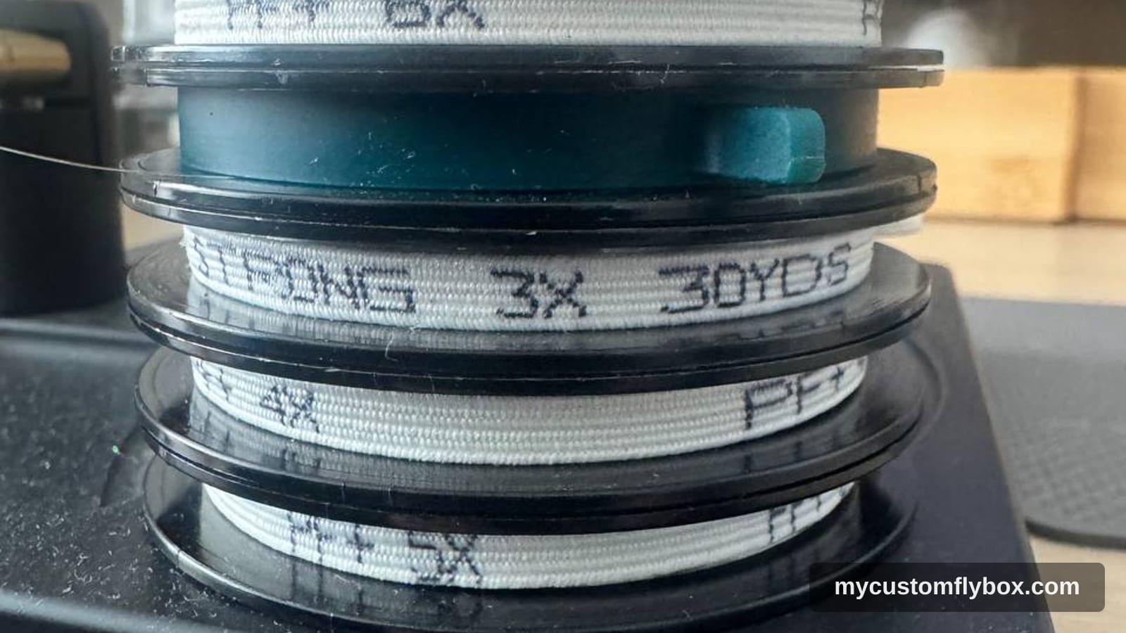 Spools of 3X tippet stacked on a fly tying bench