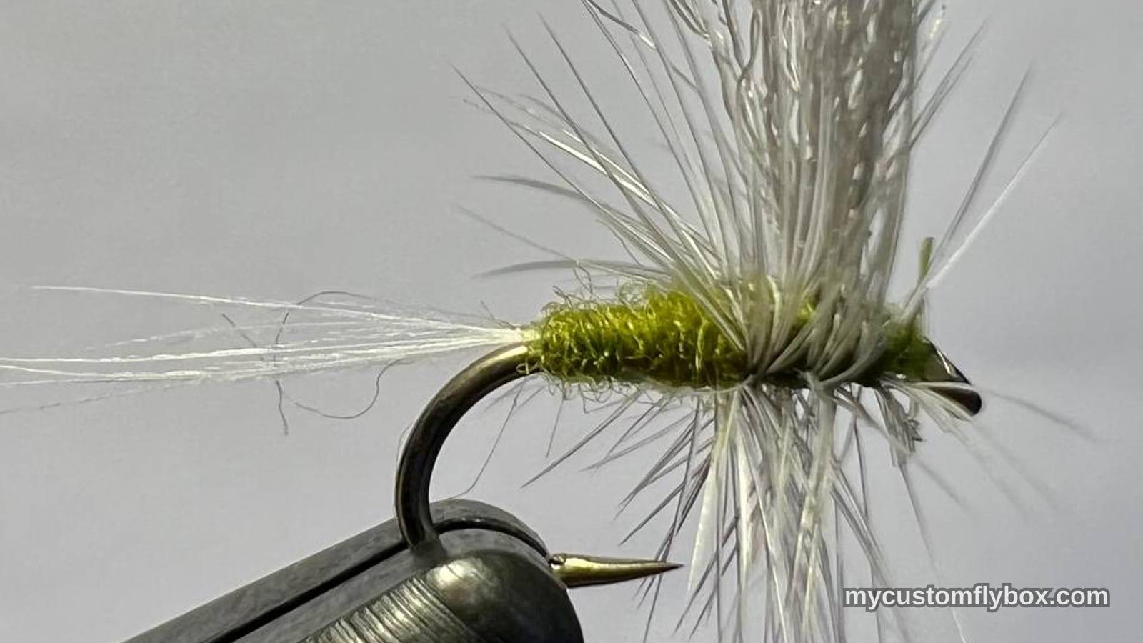 Olive-bodied dry fly with pale wing and hackle held in a tying vise