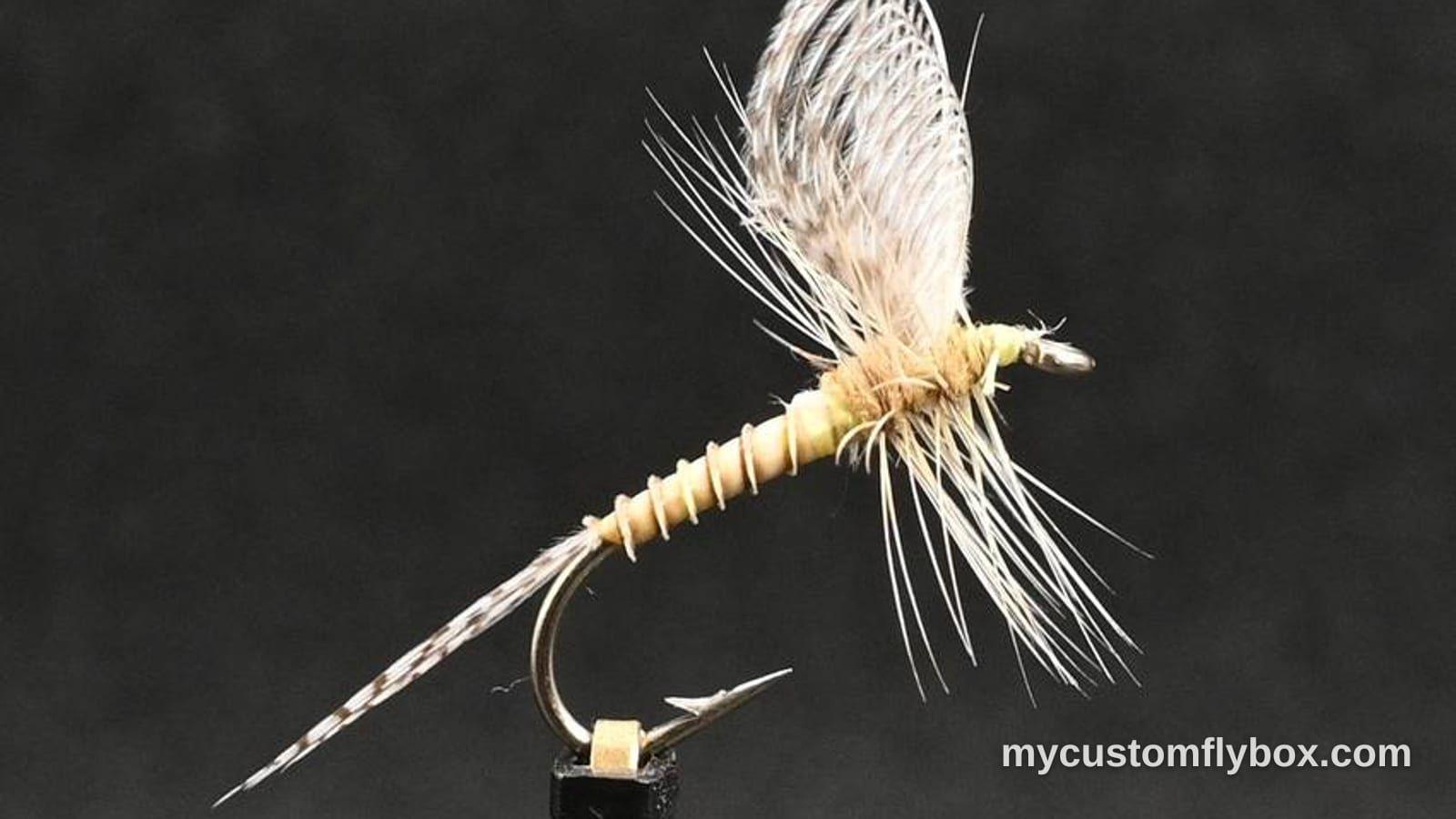 A pale mayfly dry fly tied in a vise against a dark background