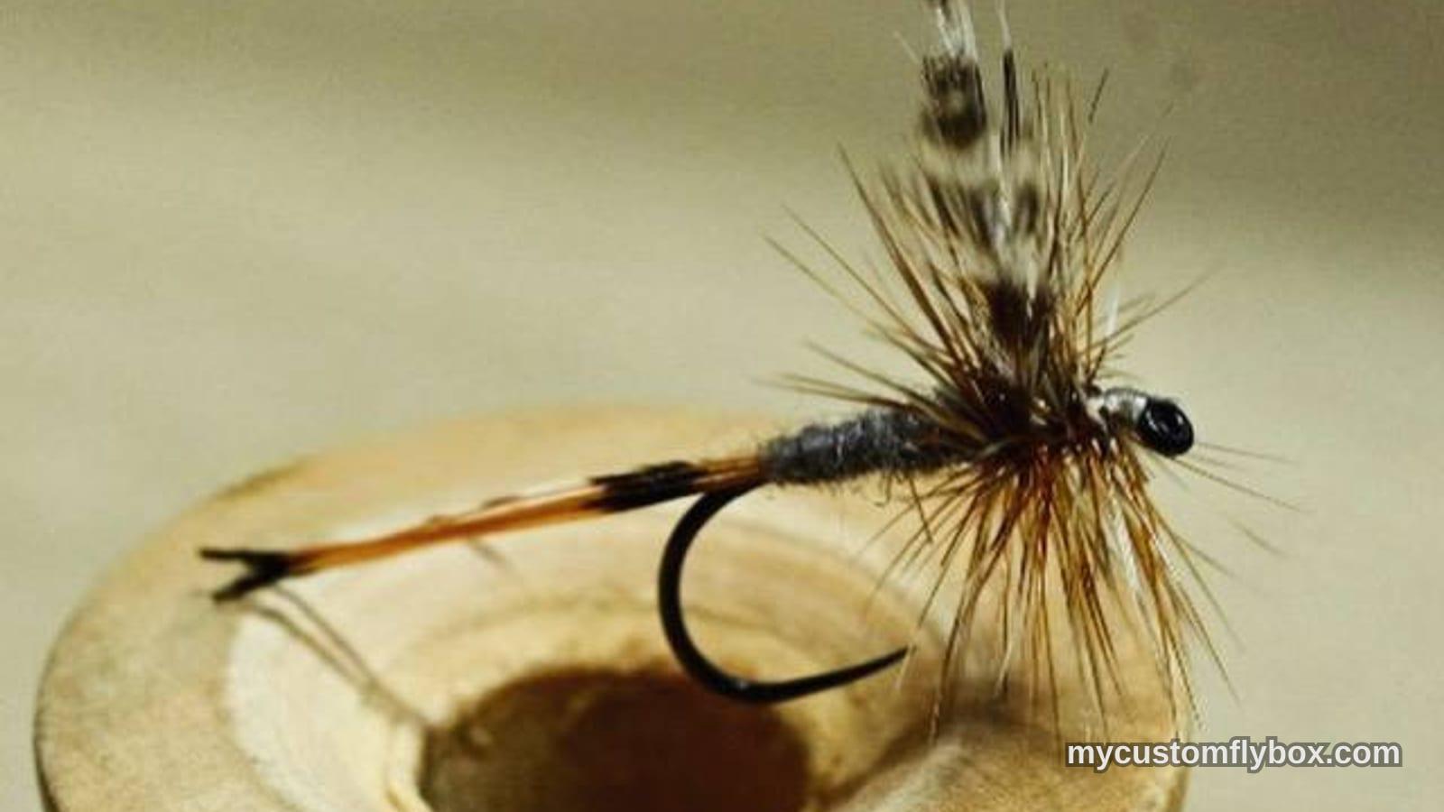 Small mayfly dry fly with upright wing tied on a wooden thread spool
