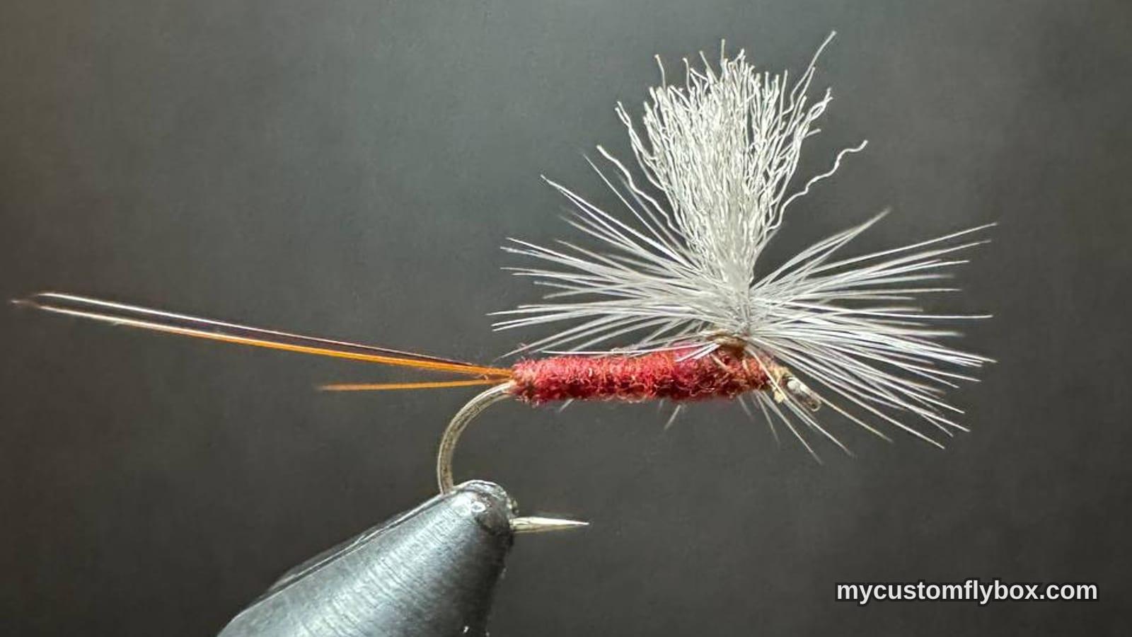 Rust-red parachute mayfly pattern held in a tying vise above thread spools