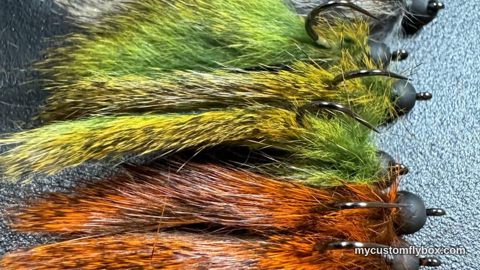 Rows of olive, tan, and rusty jig streamers arranged on a dark fly patch