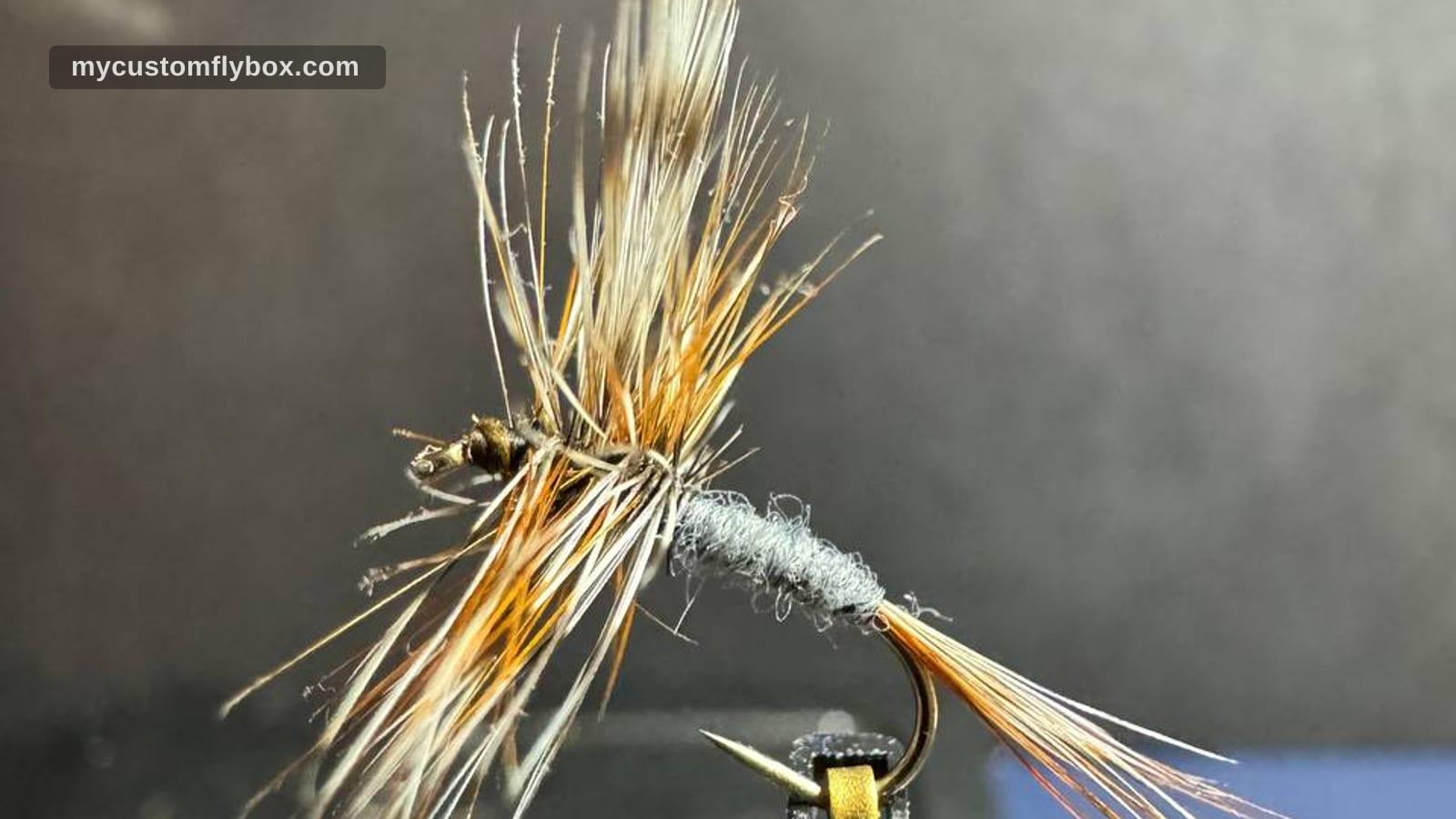 Close-up of a small gray-bodied dry fly tied in a vise