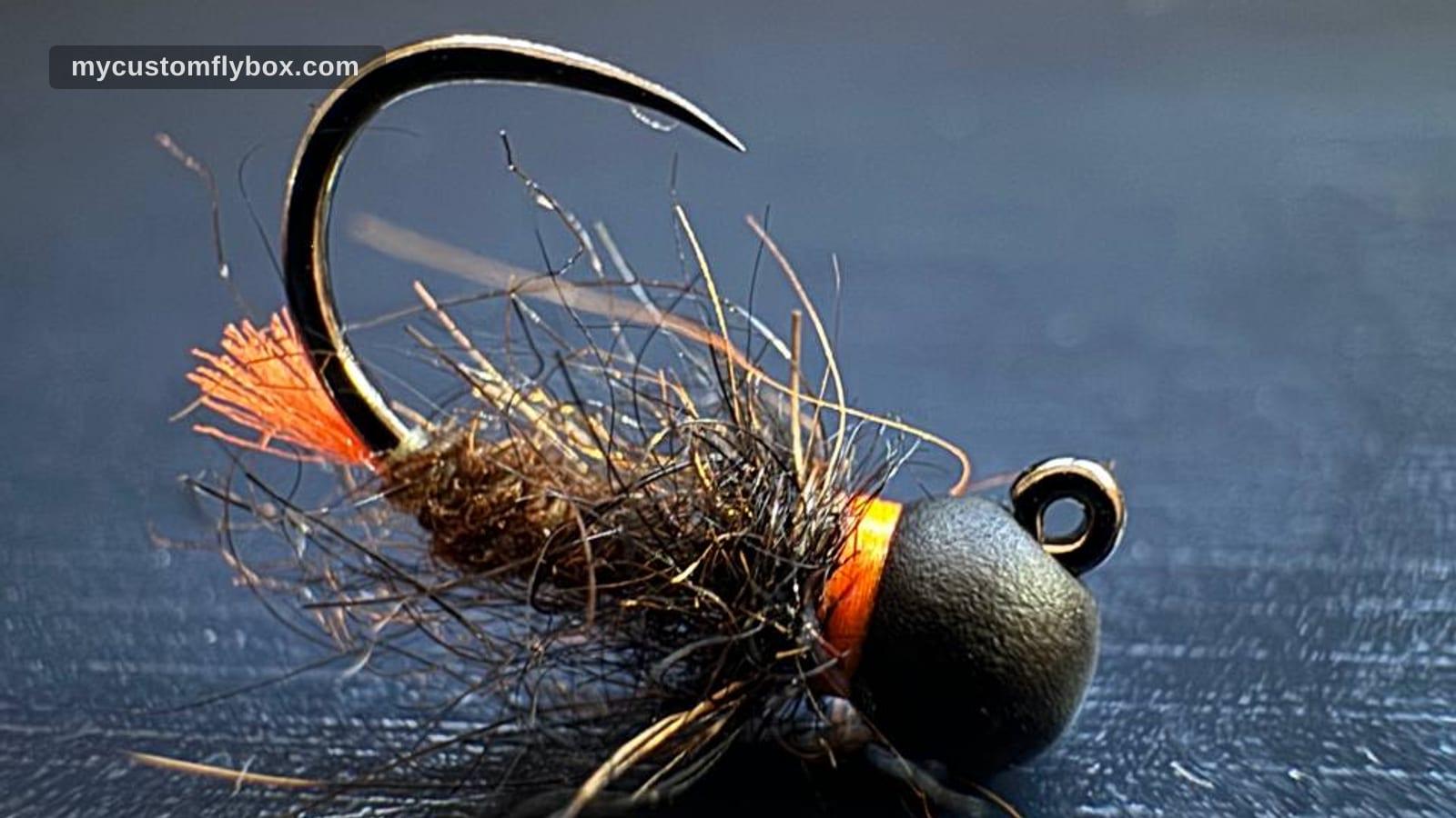 Close-up of a dark jig nymph with an orange hot spot and black bead